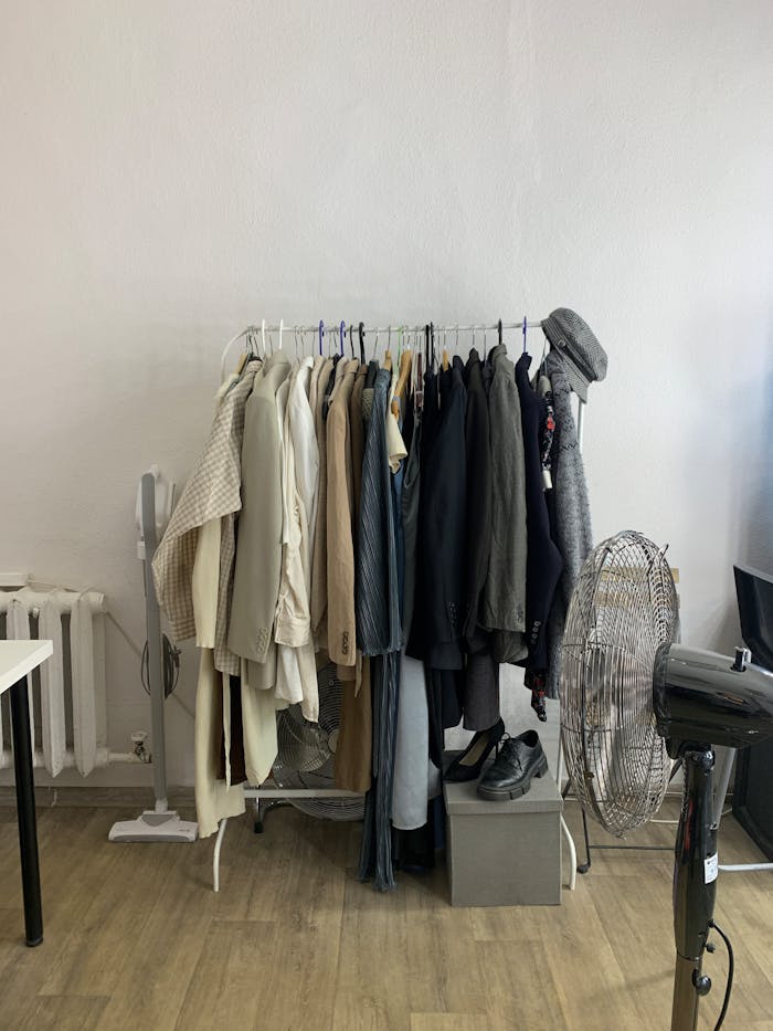 A rack of clothes in a room with a fan